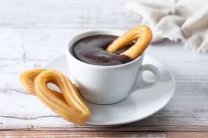 Traditional Spanish churros with hot chocolate breakfast on wooden table